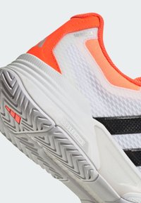 Λευκό αθλητικό παπούτσι με πορτοκαλί και μαύρο σχέδιο, υφασμάτινο πάνω μέρος και μαλακή γκρίζα σόλα με σχέδιο ψαροκόκαλο.