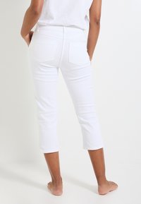Pantalones de denim blanco recortados con un diseño ajustado, que cuentan con dos bolsillos traseros y una textura suave, terminando justo debajo de la pantorrilla.