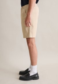 Beige cotton shorts with a flat waistband, side pockets, and a straight-leg design, paired with black loafers and white socks.