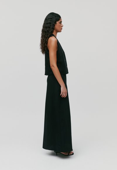 Haut sans manches noir associé à une longue jupe noire, le tout en tissu lisse. La tenue est ajustée et longue jusqu'au sol avec une silhouette fluide.