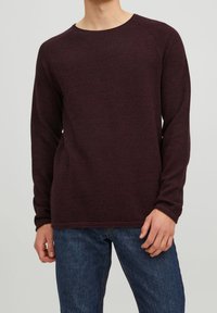 Pull-over bordeaux à manches longues avec un col rond, des poignets côtelés et un tissu texturé. Associé à un jean en denim bleu.