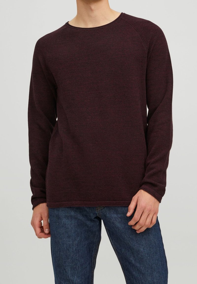 Pull-over bordeaux à manches longues avec un col rond, des poignets côtelés et un tissu texturé. Associé à un jean en denim bleu.