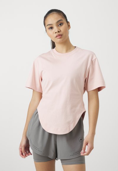 Lys rosa bomulls t-skjorte med korte ermer, rund hals og avrundet kant; kombinert med grå idrettsshorts med perforerte detaljer.
