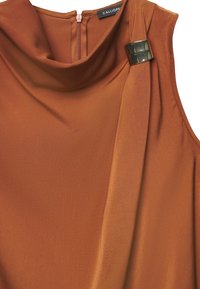 Top senza maniche color bronzo-arancione con collo a scialle, caratterizzato da un elemento decorativo in metallo nero e una discreta cerniera sul retro. Tessuto dalla texture liscia.