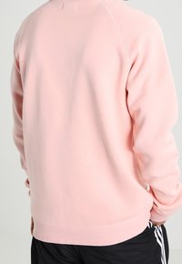 Ljusrosa sweatshirt med klassisk rund hals och ribbade muddar. Har en mjuk yta och en avslappnad passform med en ren design på baksidan.