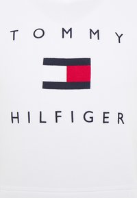 Camiseta de algodón blanca con el logotipo que presenta el texto "TOMMY HILFIGER" en negro y un diseño rectangular de bandera en rojo, blanco y azul.