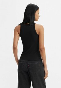 Top in cotone nero a coste con un design aderente, caratterizzato da un colletto rotondo e spalline larghe. Abbinato a jeans scuri a vita alta con tasche posteriori.