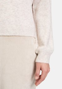Helle beige Strickjacke mit weicher Textur, gerippten Bündchen und leicht oversize Passform, kombiniert mit beige gerippten Hosen.