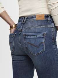 Mørkeblå denimjeans med en tettsittende form, synlige baklommer og et lærlogo-patch med merket "ONLY." Kontraststrikking detaljer.