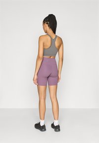 Αθλητική ενδυμασία περιλαμβάνει γκρι αθλητικό σουτιέν και μωβ σορτς με ψηλή μέση, κατασκευασμένα από λείο ύφασμα. Μαύρα παπούτσια με λευκές κάλτσες ολοκληρώνουν την εμφάνιση.