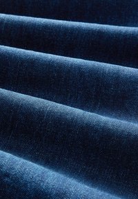 Gros plan d’un tissu denim bleu foncé plié montrant la texture et le motif de tissage.