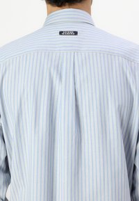 Camicia a righe blu chiaro realizzata in tessuto; presenta un yoke posteriore e un'etichetta con la scritta "GUESS MARINE", evidenziando sottili linee verticali.