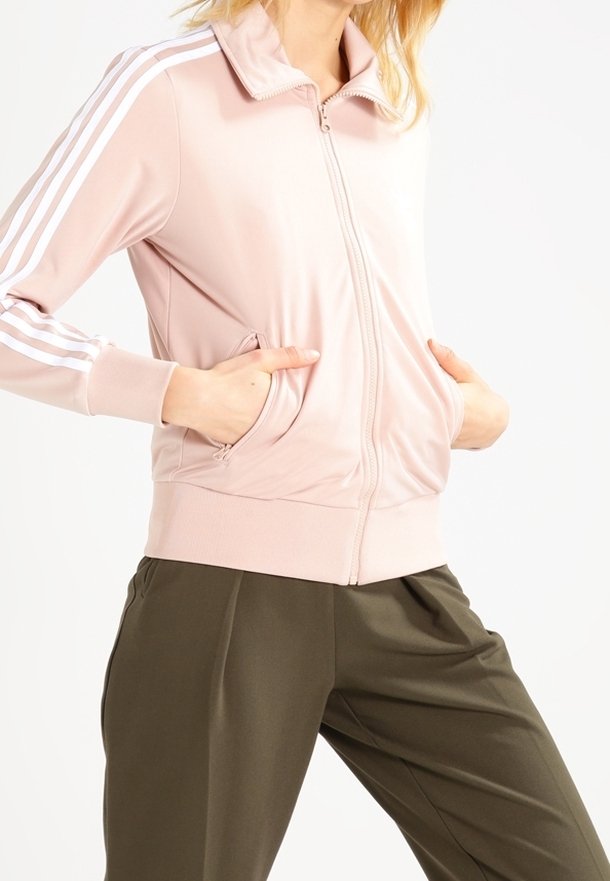 Rosa zip-up jacka med vita ränder på ärmarna, framtida fickor och en mjuk, slät textur. Matchad med lösa olivgröna byxor.