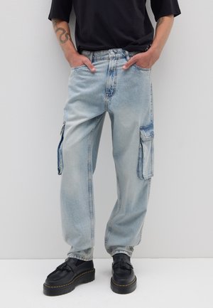 Light blue cargo jeans featuring a loose fit, elastic waistband, side pockets, and a faded texture. Paired with black platform shoes.