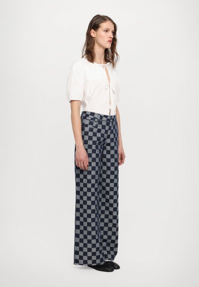 Weißes Kurzarmoberteil mit Krawattenverschluss; blau-graue karierte weite Hosen mit Taschen; glatte Textur und fließende Silhouette.
