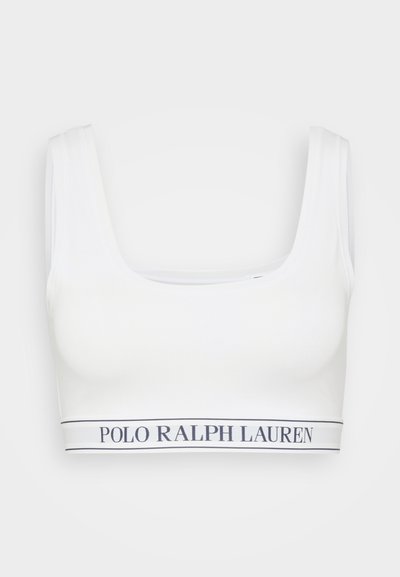 Hvit bralette med vid, utringet halslinje og tykke stropper. Den har et kontrasterende logobånd nederst i marineblå. Myk og elastisk stoff.