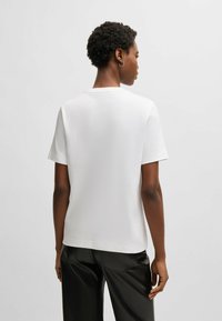 T-shirt bianca a maniche corte in morbido cotone, con collo rotondo classico e orlo dritto, abbinata a pantaloni di pelle nera.