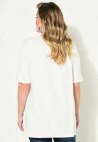 Vit kortärmad topp som visas bakifrån, med en avslappnad passform och sidsprund, i ett mjukt och lätt tyg samt med rundad nedre kant.