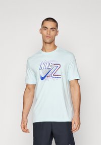 Camiseta corta de Nike de color azul claro con mangas cortas, que presenta un logo gráfico multicolor con rayas y acentos circulares, hecha de una tela suave.