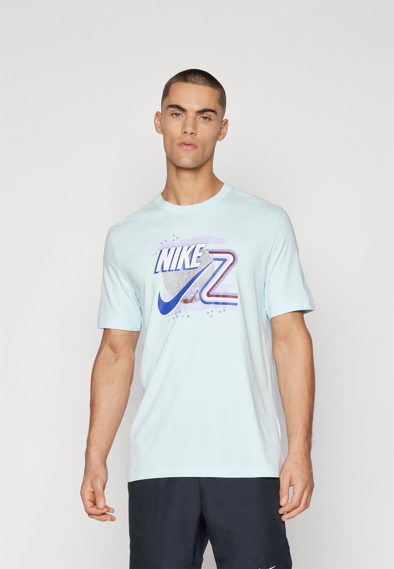 Camiseta corta de Nike de color azul claro con mangas cortas, que presenta un logo gráfico multicolor con rayas y acentos circulares, hecha de una tela suave.