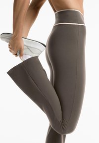 Hochgeschnittene, braune Sportlegging mit einer glatten Textur und kontrastierendem hellen Besatz, die eine enge Passform für Flexibilität bietet.