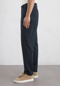 Navyblaue Hosen mit geradem Schnitt, aus einem glatten Stoff. Mit vorderen Taschen und einer geknöpften Gesäßtasche. Kombiniert mit beigen Sneakers.