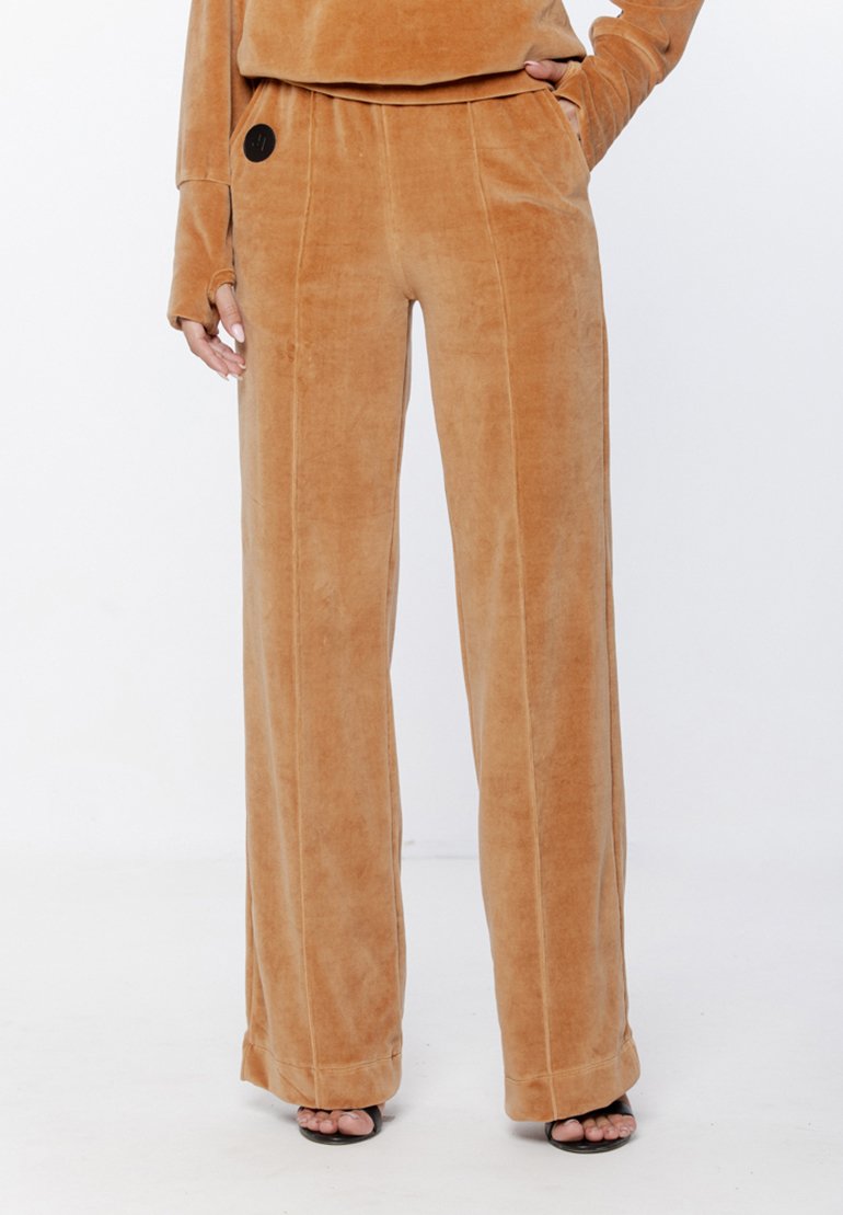 Spodnie z szerokimi nogawkami, wykonane z miękkiego, puszystego materiału w ciepłym beżowym kolorze. Posiadają czarny okrągły akcent w talii oraz bezszwowe szwy.