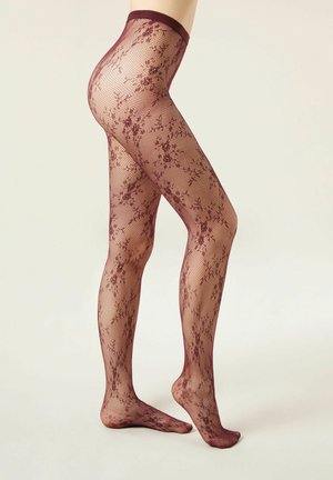 Jambes portant des collants transparents à motif de dentelle florale bordeaux avec une ceinture renforcée, se tenant sur la pointe des pieds sur un fond uni.