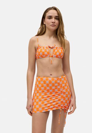 Top de bikini con patrón naranja y lazo ajustable, combinado con una falda arrugada a juego con detalles de cuerda. Material suave y elástico.