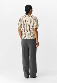 Haut crème avec des lignes ondulées noires, manches courtes bouffantes. Pantalons larges gris. Tissu lisse avec une coupe décontractée. Pas de matériel ou d'accents notables.