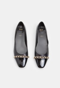 Black patent leather flats with a rounded toe and a decorative gold chain accent across the front. Smooth interior lining.