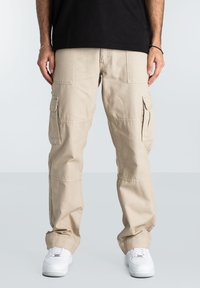 Beige cargo pants with side pockets, straight legs, and slight tapering at the ankles, paired with white sneakers and a black t-shirt.