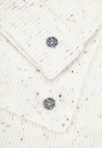 Biała prążkowana dzianina z wielokolorowymi kropkami, ozdobiona dwoma okrągłymi srebrnymi guzikami, z których każdy ma wytłoczony wzór gwiazdy.