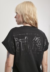 Crna oversized majica s poderanim rukavima, koja na stražnjoj strani ima velike grafičke printove u sjajnom finishu, s natpisom "do it for the".