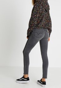 Jeans skinny grigi con dettagli a zip laterale, abbinati a un hoodie nero con motivo. Indossati con sneaker nere con accenti bianchi.