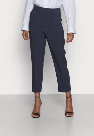 Maritieme op maat gemaakte broek met een hoge taille, voorzien van een slank ontwerp, zachte textuur en verkorte lengte. Gecombineerd met zwarte haksandalen.