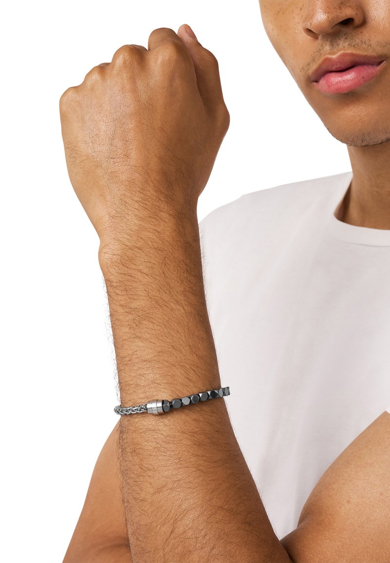Bracelet en perles noires avec une chaîne grise tressée et des accents métalliques, mettant en valeur un mélange de textures et de formes géométriques.