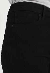 Vaqueros de mezclilla negra con un diseño ajustado, que presentan una cintura alta, bolsillos traseros y detalles de costura sutiles. Textura suave.