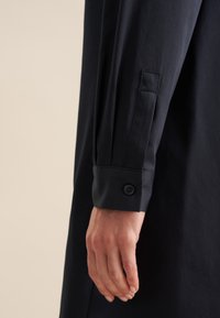 Maglietta nera a manica lunga, con polsino abbottonato e tessuto liscio, che mette in risalto il design senza cuciture e la vestibilità sartoriale.