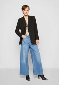 Blazer nero doppiopetto su una maglietta a fantasia, abbinato a jeans larghi blu chiaro e stivaletti neri con tacco.