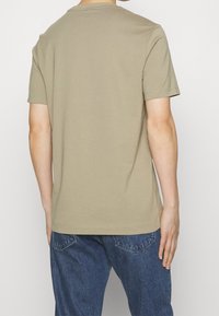 Kortärmad, beige bomullströja med rund halsringning. Enkel design, mjuk textur och normal passform. Bärs med mörkblå denimjeans.