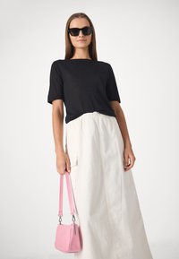 Black short-sleeve top paired with a white, floor-length skirt. Holding a small pink handbag with a shoulder strap, featuring a smooth texture.