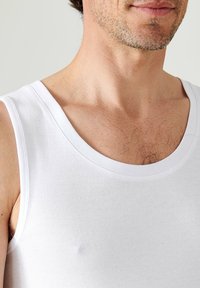 White cotton tank top with a ribbed texture, wide scoop neckline, and clean edge stitching, featuring no visible patterns or accents.