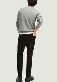Suéter gris de punto, pantalones negros y zapatos negros. El suéter presenta una textura acanalada, mangas largas y un diseño ajustado.
