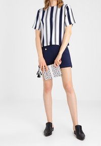 Haut à manches courtes rayé bleu marine et blanc, associé à un short bleu marine. Pochette transparente avec un motif. Chaussures noires faciles à enfiler.