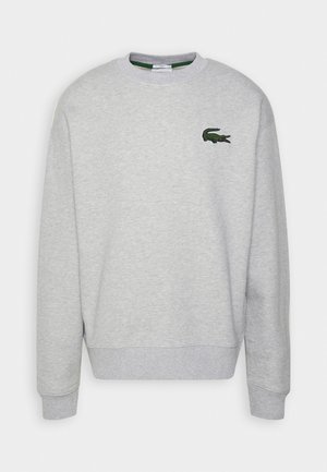 Sweat-shirt gris en tissu doux, avec un col rond, des poignets côtelés et un petit logo crocodile vert brodé sur la poitrine.