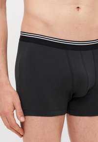 Schwarze Boxershorts mit einer weichen Textur und einer körpernahen Passform. Mit einem schwarzen Bündchen, das zwei weiße Streifen hat.