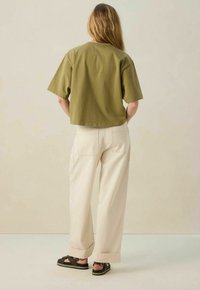 T-shirt vert olive court à manches courtes, associé à un pantalon large crème avec poches arrière et finitions roulées. Sandales noires à brides.