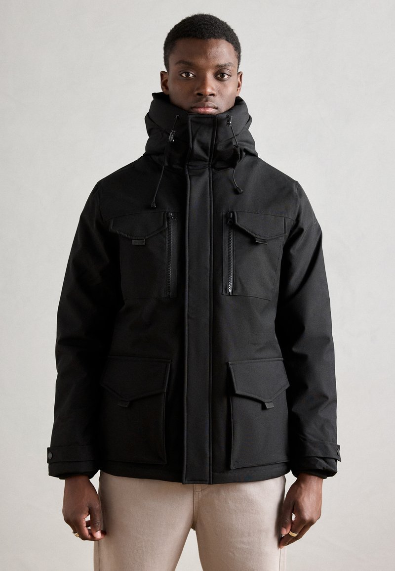 Chaqueta de invierno negra con un collar alto, dos bolsillos en el pecho con cremalleras y dos bolsillos delanteros con tapa. Fabricada con una tela suave y texturizada.