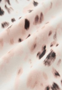 Tissu doux avec des taches noires et beiges irrégulières sur fond blanc, ressemblant à un motif subtil d'imprimé animal.